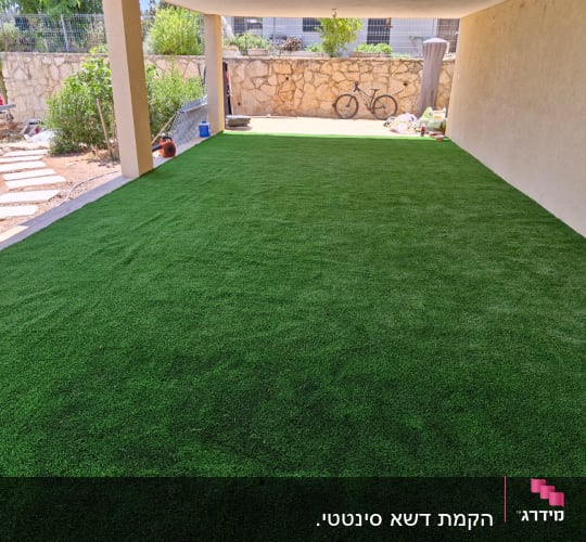 דשא סינתטי פרוס בחצר עם כלי גינון בצד